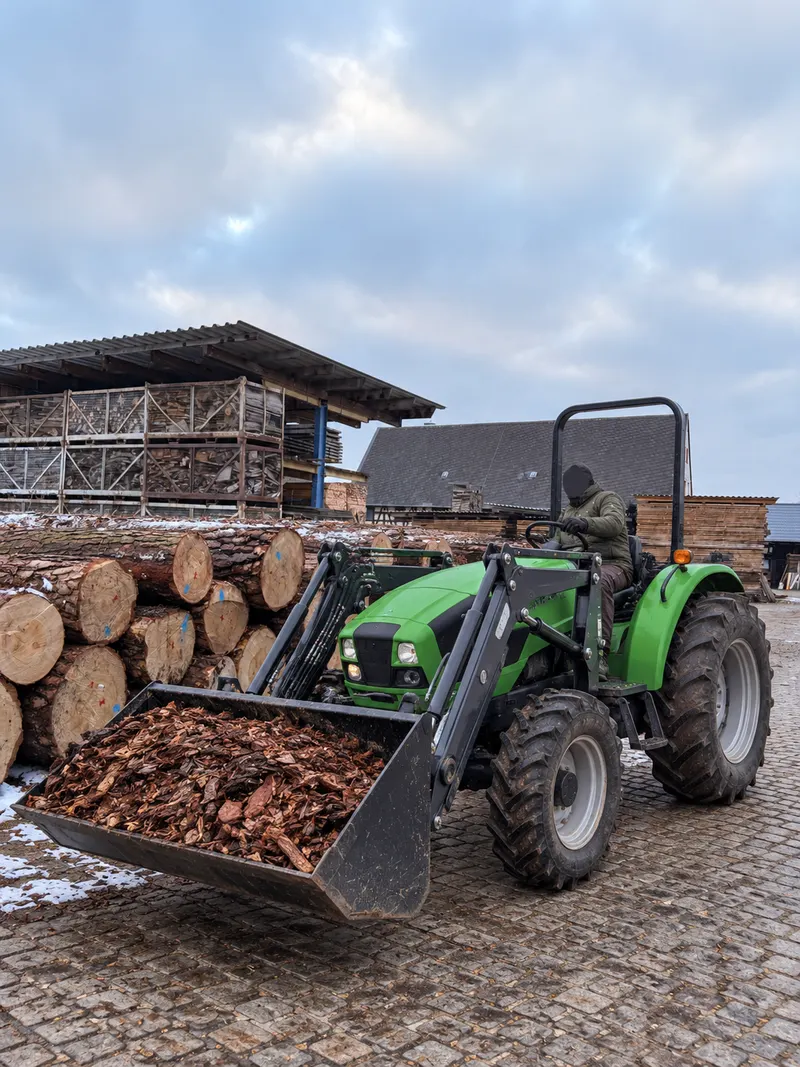 Traktor mit Frontlader beim Beladen von Rindenmulch auf dem Holzplatz